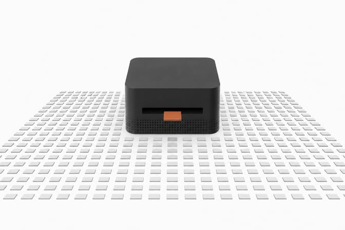 A thick, square desktop computer sits at the center of a vast, precise grid of small blank tiles, with a single accented tile entering its front slot to represent a local AI inference query.